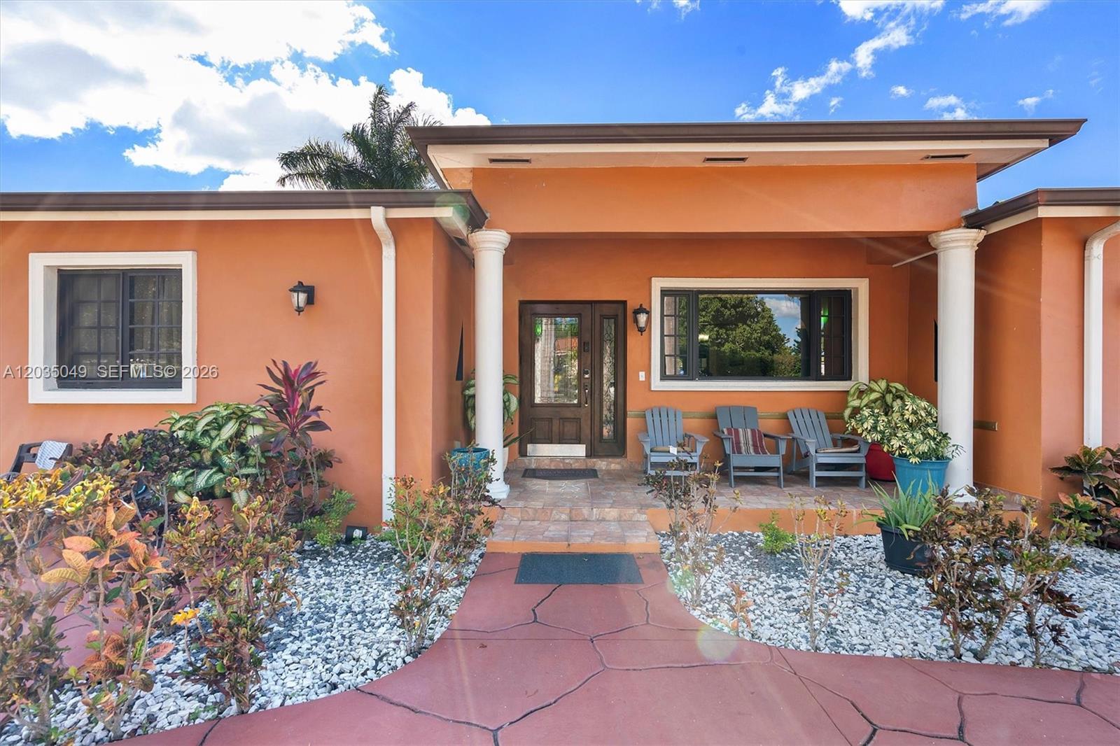 The exterior of an orange house features a covered porch with three chairs and columns — 348 NE 118th St, Miami FL 33161, MIAMI, FL