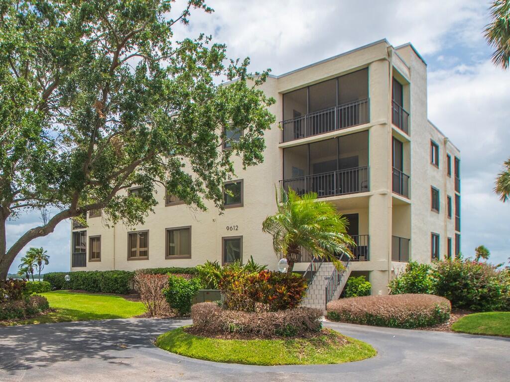 A three-story apartment building with screened balconies stands behind a circular driveway and landscaping — 9612 Riverside Drive # 203, Sebastian FL 32958, SEBASTIAN, FL