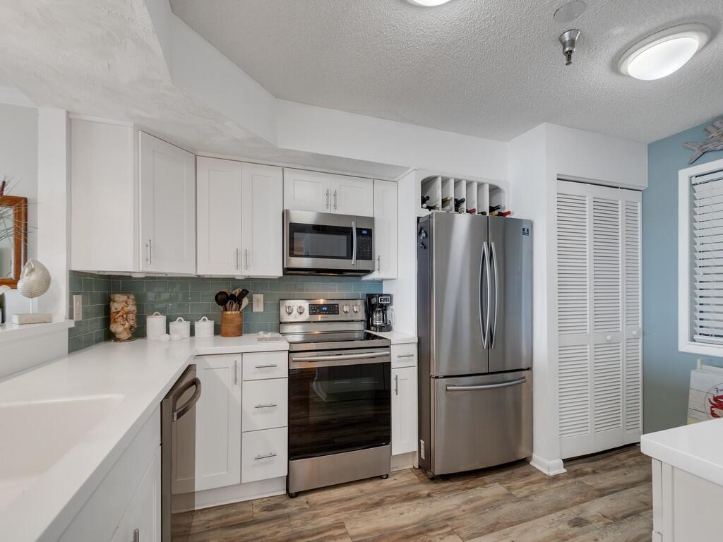 A kitchen features white cabinets, stainless steel appliances, a blue tile backsplash, and wood flooring — 9612 Riverside Drive # 203, Sebastian FL 32958, SEBASTIAN, FL