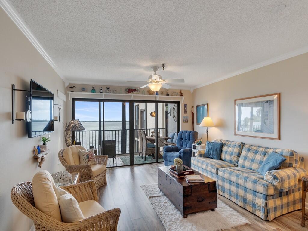 A living room features a blue plaid sofa, wicker chairs, a wooden chest, and balcony views — 9612 Riverside Drive # 203, Sebastian FL 32958, SEBASTIAN, FL