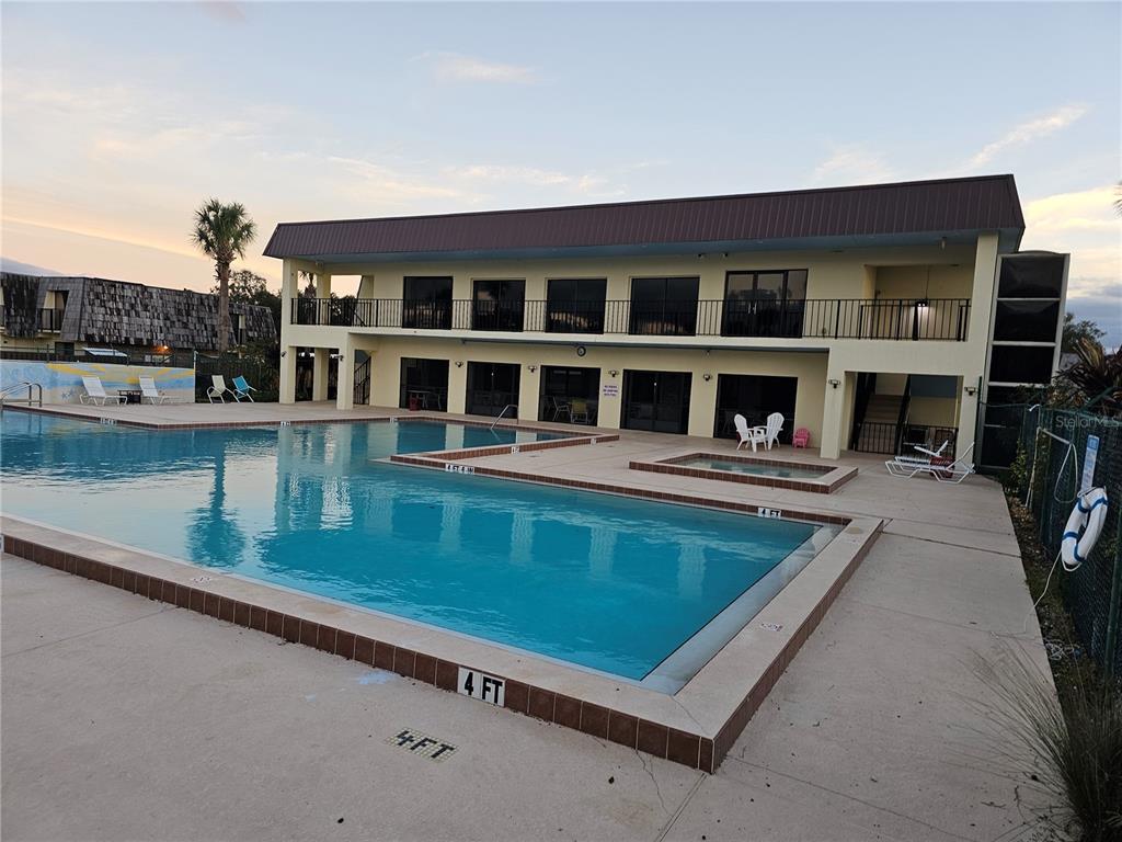 A rectangular swimming pool sits in front of a two-story building with a brown roof — 2927 TANGERINE COURT, LEESBURG, FL