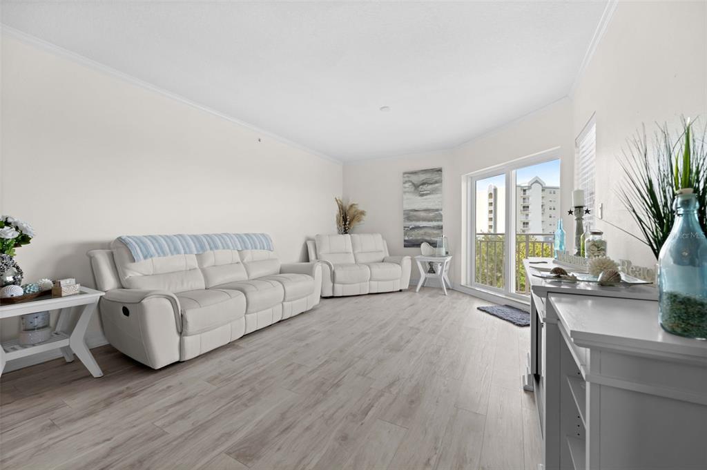 A bright living room features white leather sofas, light wood-look flooring, and a sliding glass door — 4516 SEAGULL DRIVE UNIT 419, NEW PORT RICHEY, FL
