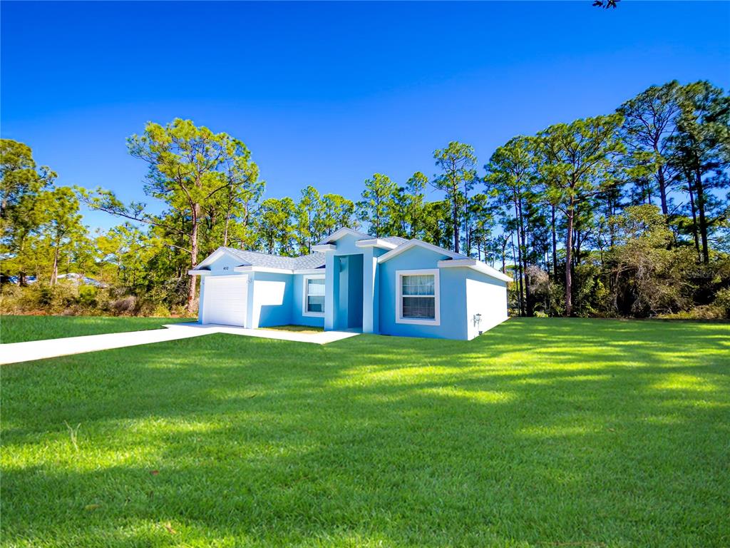A single-story blue house with a white garage sits on a large grassy lot — 450 KEMPER AVENUE, LAKE PLACID, FL