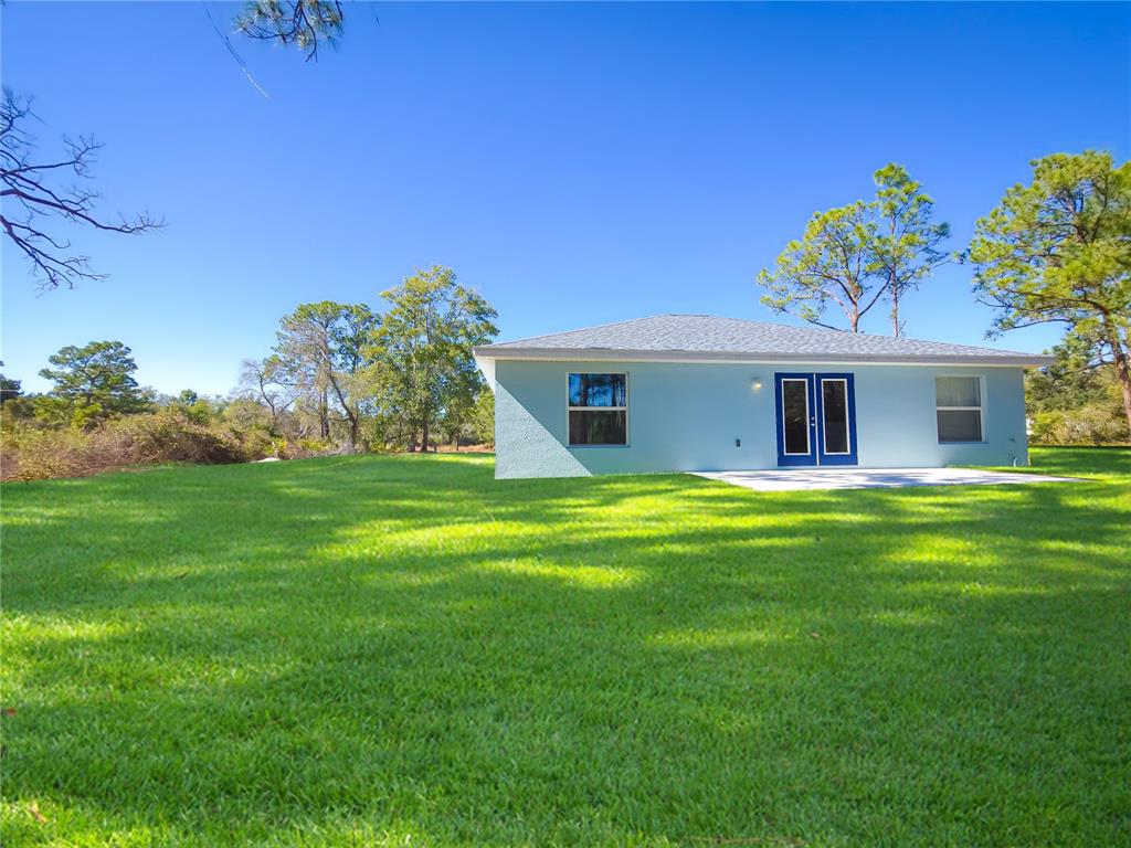 A light blue house with a concrete patio sits on a large, grassy lawn — 450 KEMPER AVENUE, LAKE PLACID, FL