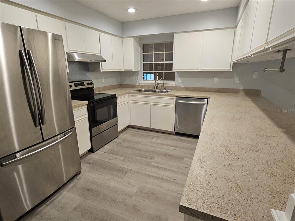 A kitchen features white cabinets, stainless steel appliances, light countertops, and wood-look flooring — 22360 SOUTHSHORE DRIVE, LAND O LAKES, FL
