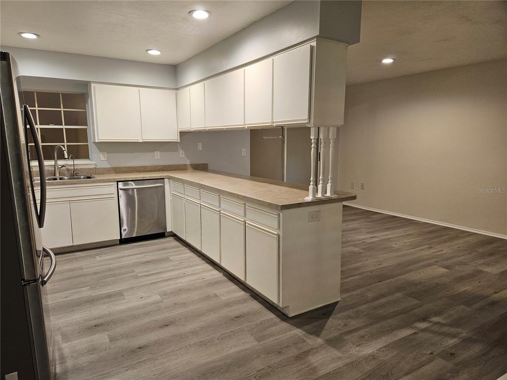 A kitchen with white cabinets, stainless steel appliances, and wood-look flooring opens to a room — 22360 SOUTHSHORE DRIVE, LAND O LAKES, FL
