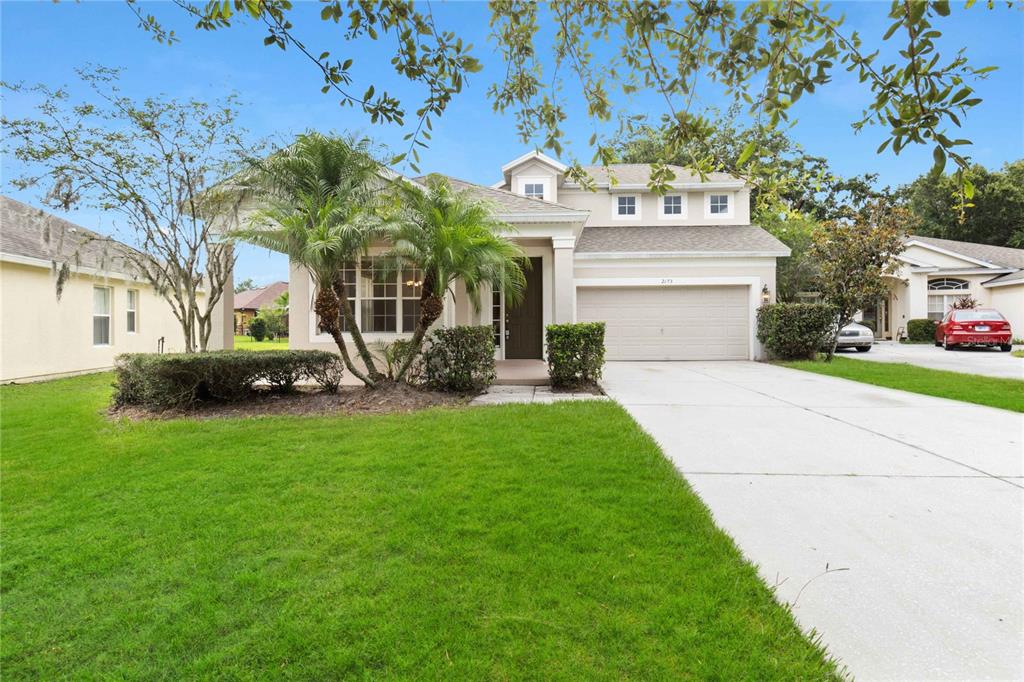 A two-story suburban house with a beige exterior, a two-car garage, and a palm tree — 2173 GRANGER AVENUE, KISSIMMEE, FL
