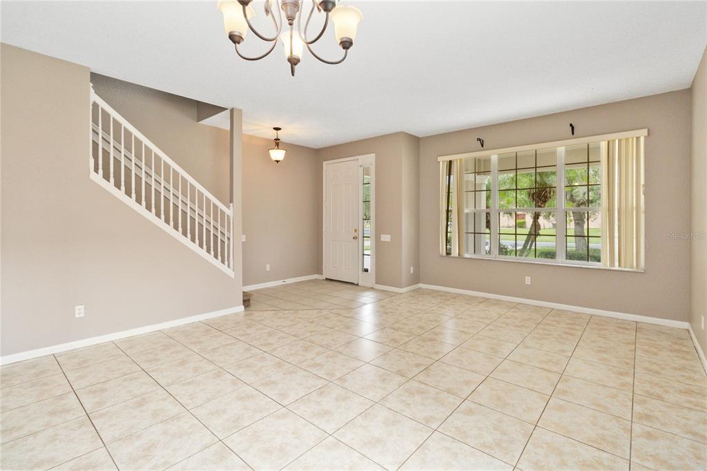 A bright living area features beige tile flooring, a staircase with white railings, and large windows — 2173 GRANGER AVENUE, KISSIMMEE, FL