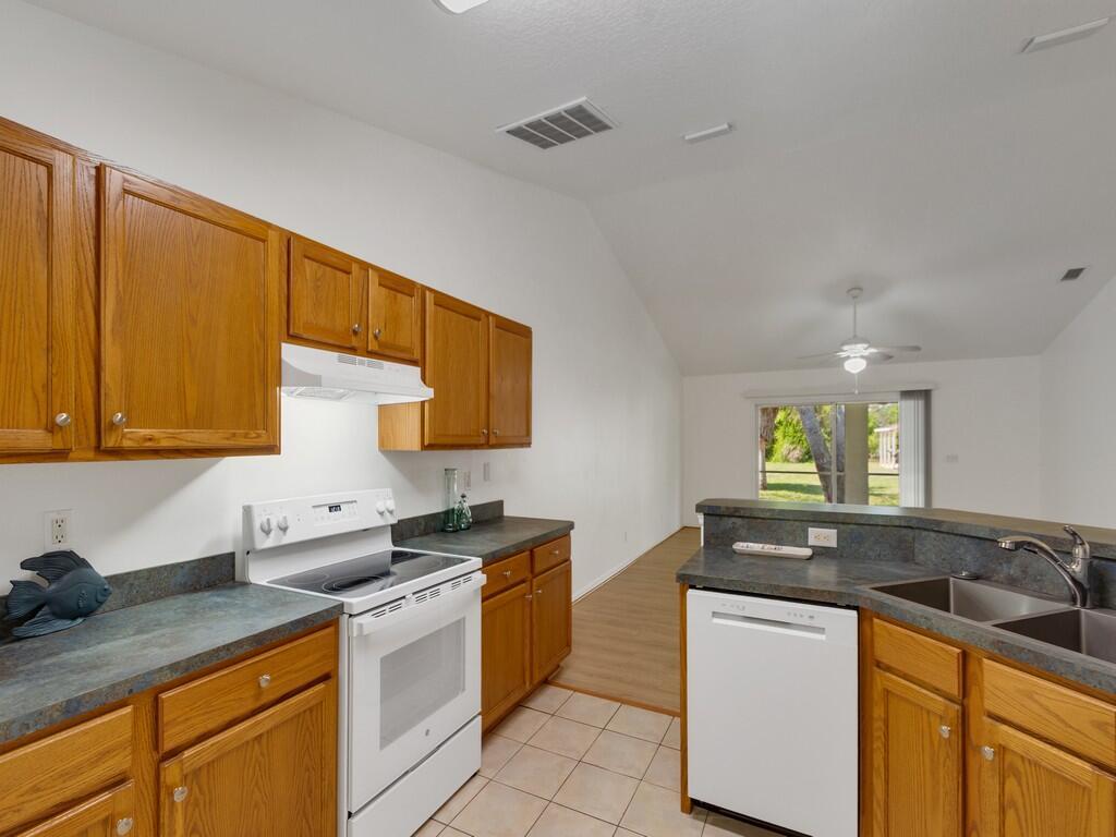 A kitchen with oak cabinets, dark countertops, white appliances, and tiled flooring — 11171 Airport Drive, Sebastian FL 32958, SEBASTIAN, FL