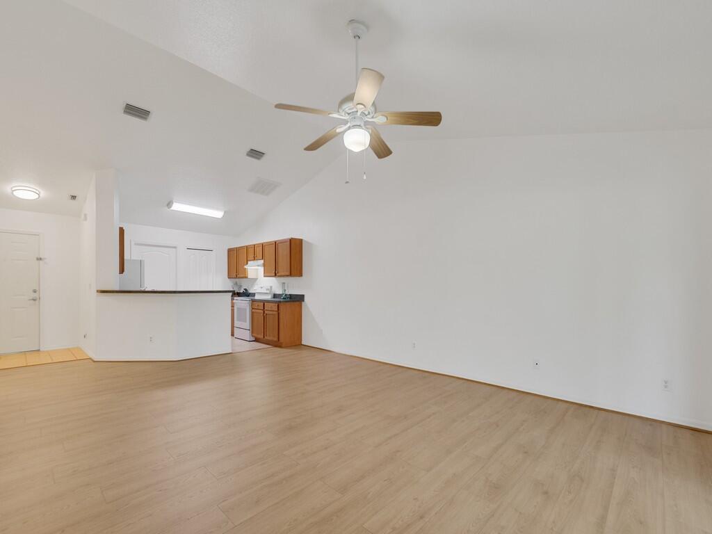 An open-concept living area features light wood-look flooring, a vaulted ceiling, and a kitchen — 11171 Airport Drive, Sebastian FL 32958, SEBASTIAN, FL