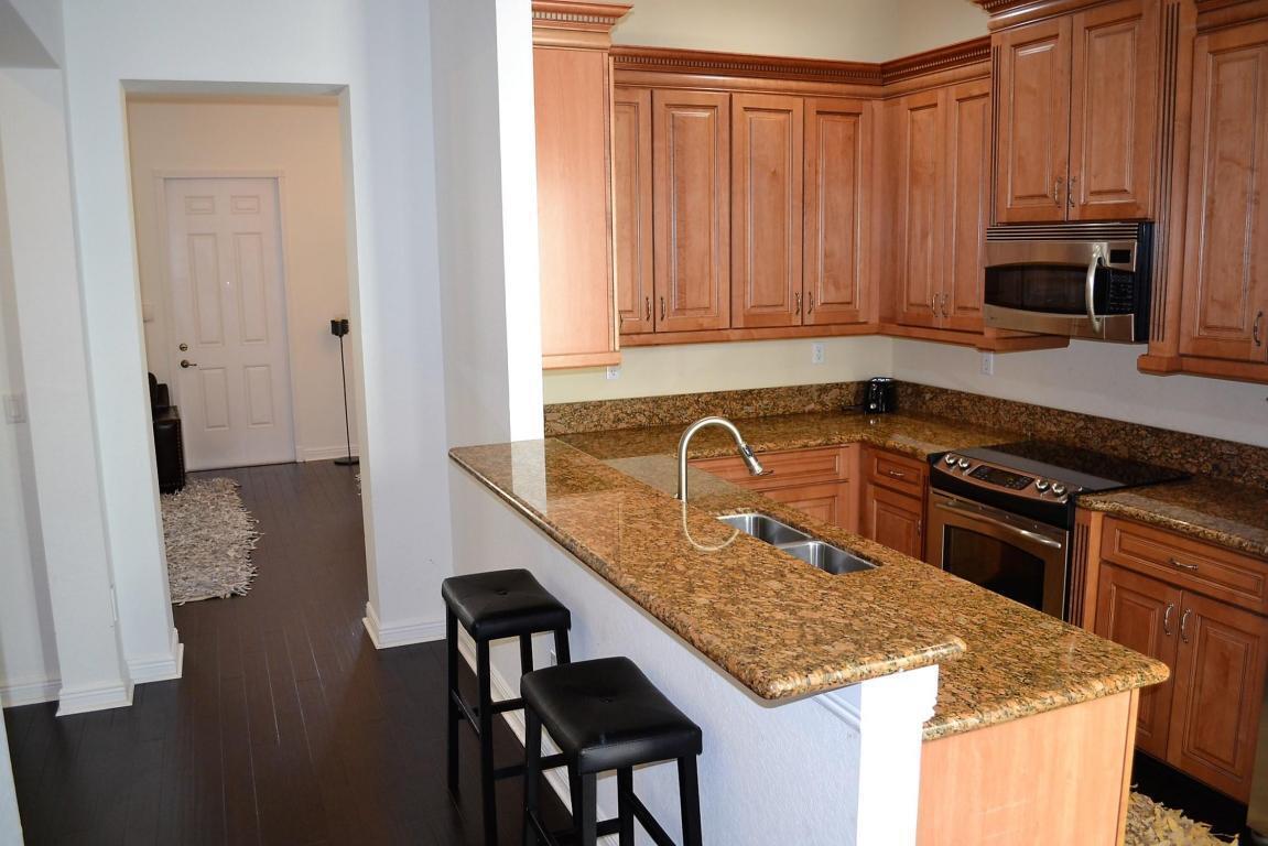 A kitchen with wood cabinets, granite countertops, and a breakfast bar with two black stools — 8305 NW 7th Court, Boca Raton FL 33487, BOCA RATON, FL