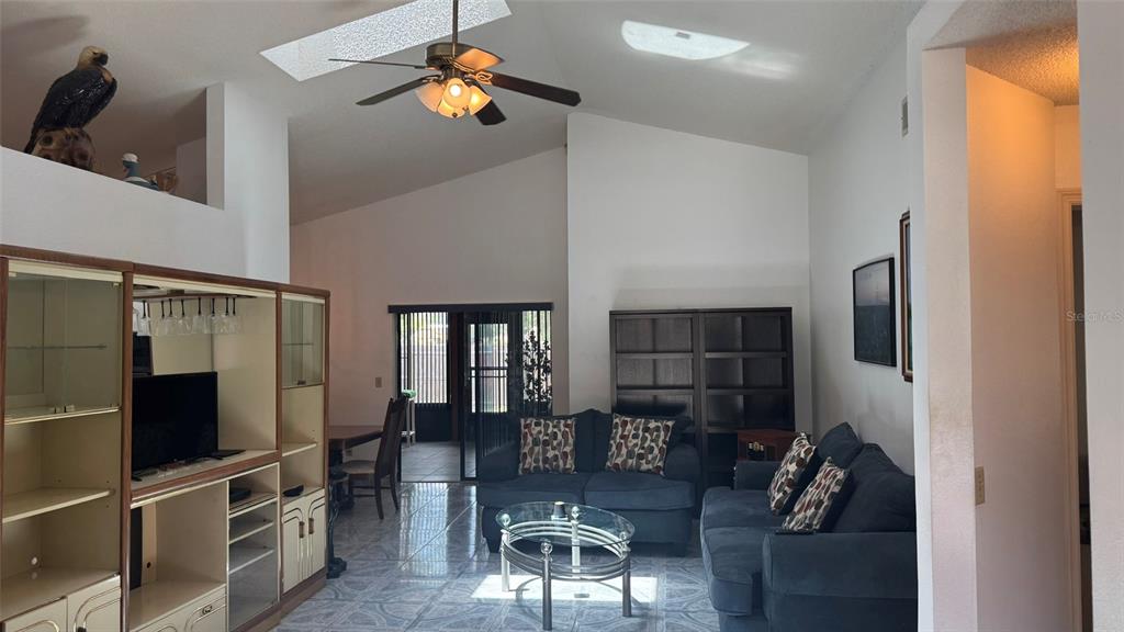A living room with vaulted ceilings, a ceiling fan, tiled floors, and dark blue sofas — 265 RIVER CHASE DRIVE, ORLANDO, FL