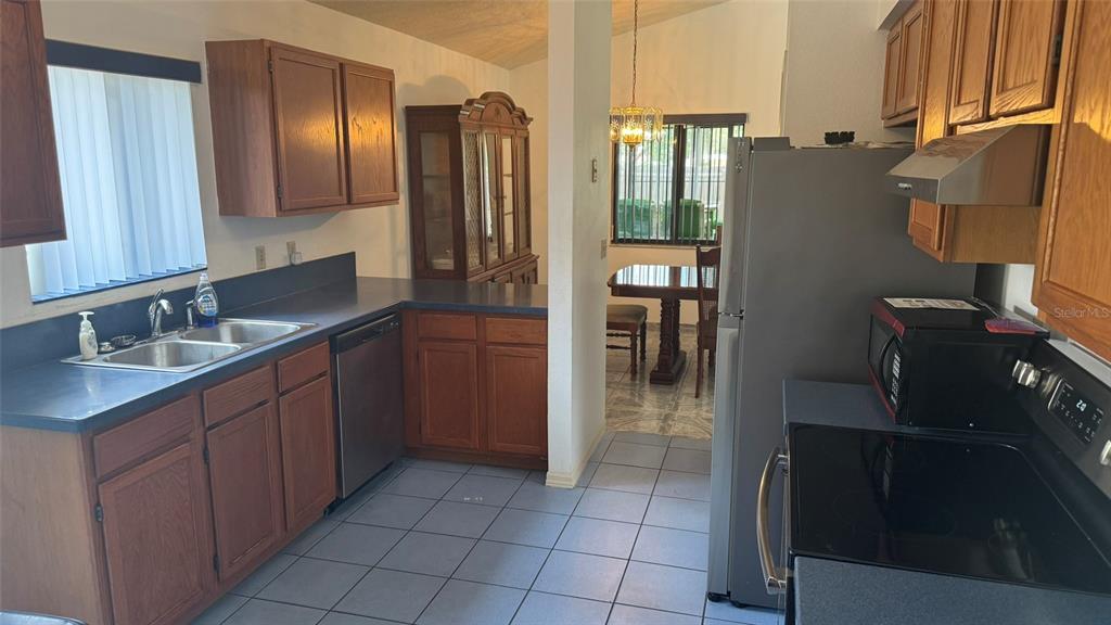A kitchen with wood cabinets, dark countertops, stainless steel appliances, and blue tile flooring — 265 RIVER CHASE DRIVE, ORLANDO, FL