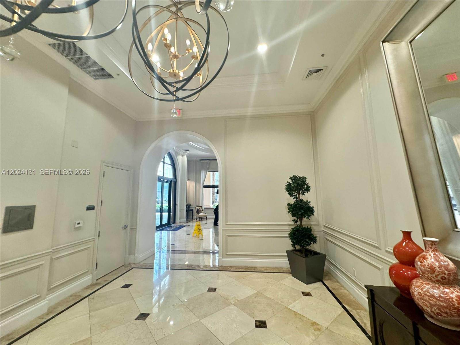A bright, tiled foyer features a large chandelier, an arched entryway, and a potted topiary — 55 Merrick Way # 831, Coral Gables FL 33134, CORAL GABLES, FL