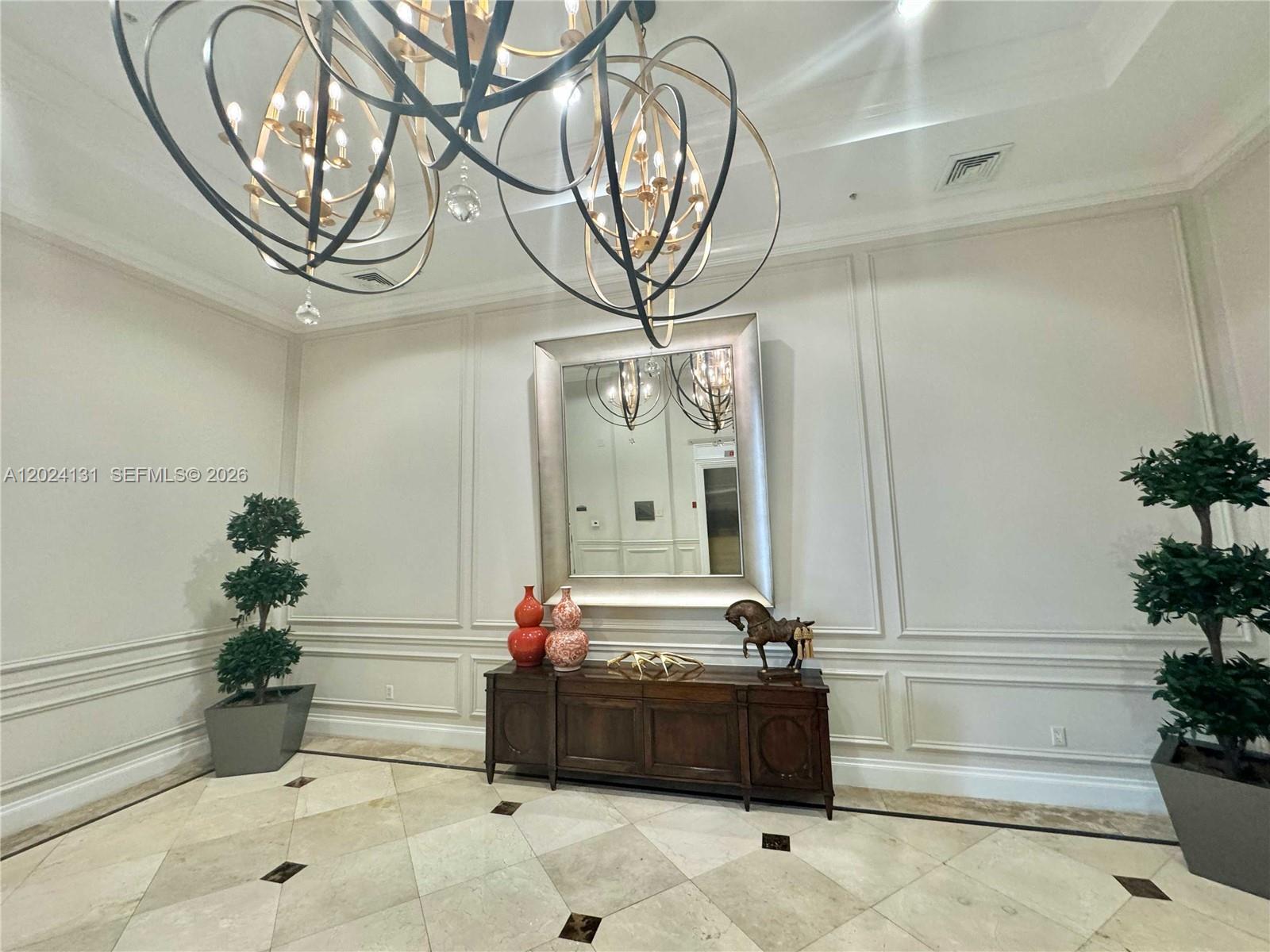 A formal lobby features a large chandelier, a central mirror, and two potted topiary trees — 55 Merrick Way # 831, Coral Gables FL 33134, CORAL GABLES, FL