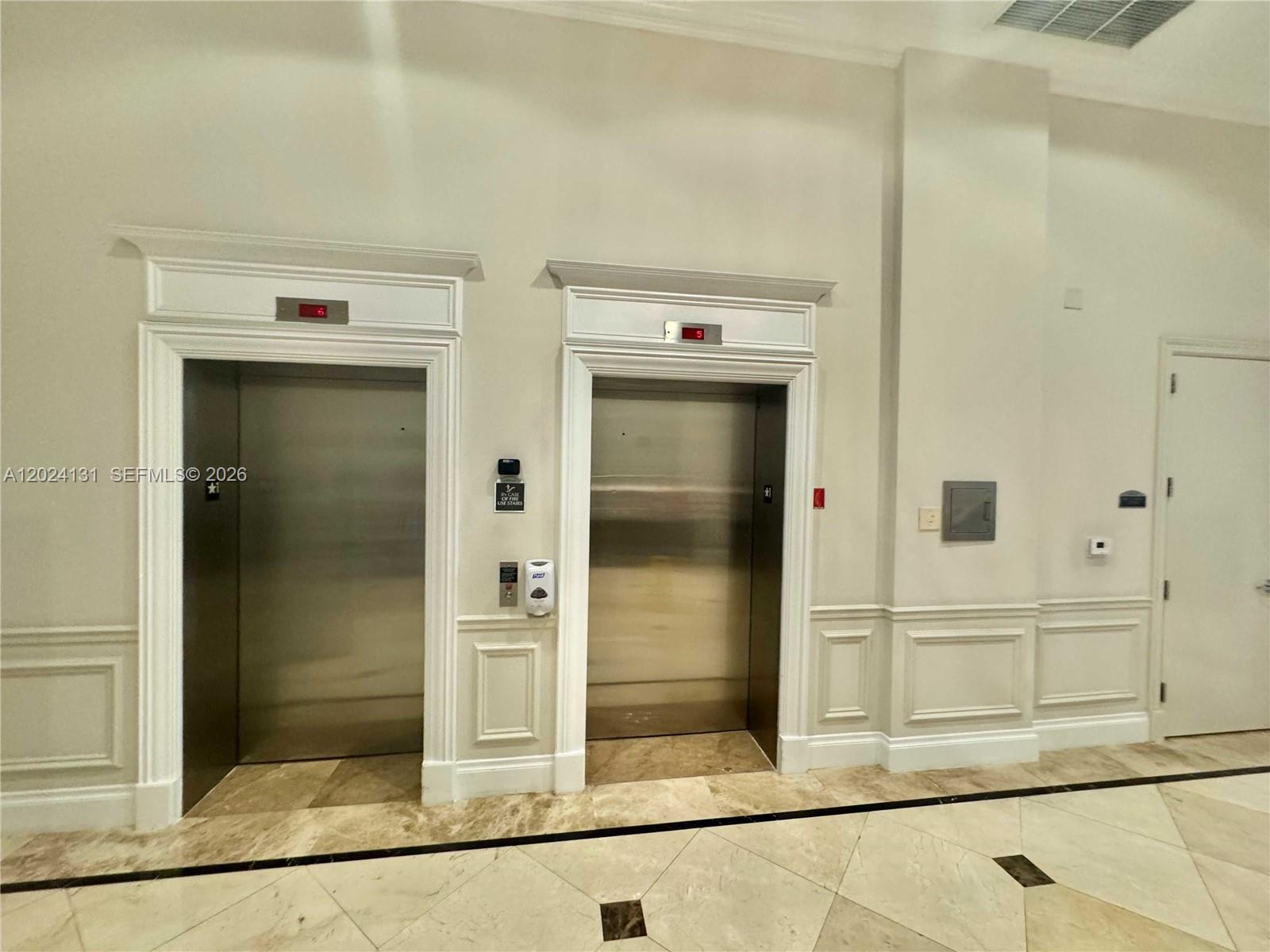 Two stainless steel elevators are set into a wall with white molding and marble flooring — 55 Merrick Way # 831, Coral Gables FL 33134, CORAL GABLES, FL
