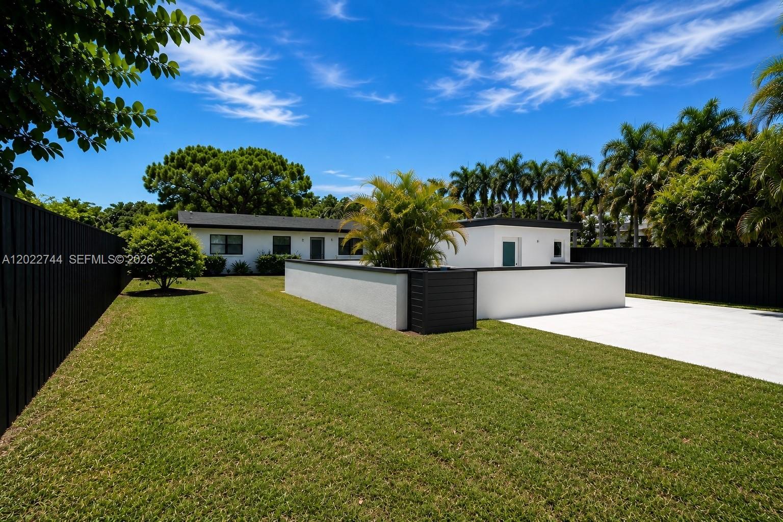 A white house with a flat roof and a fenced yard under a blue sky — 2573 Conroy Dr, North Palm Beach FL 33403, NORTH PALM BEACH, FL