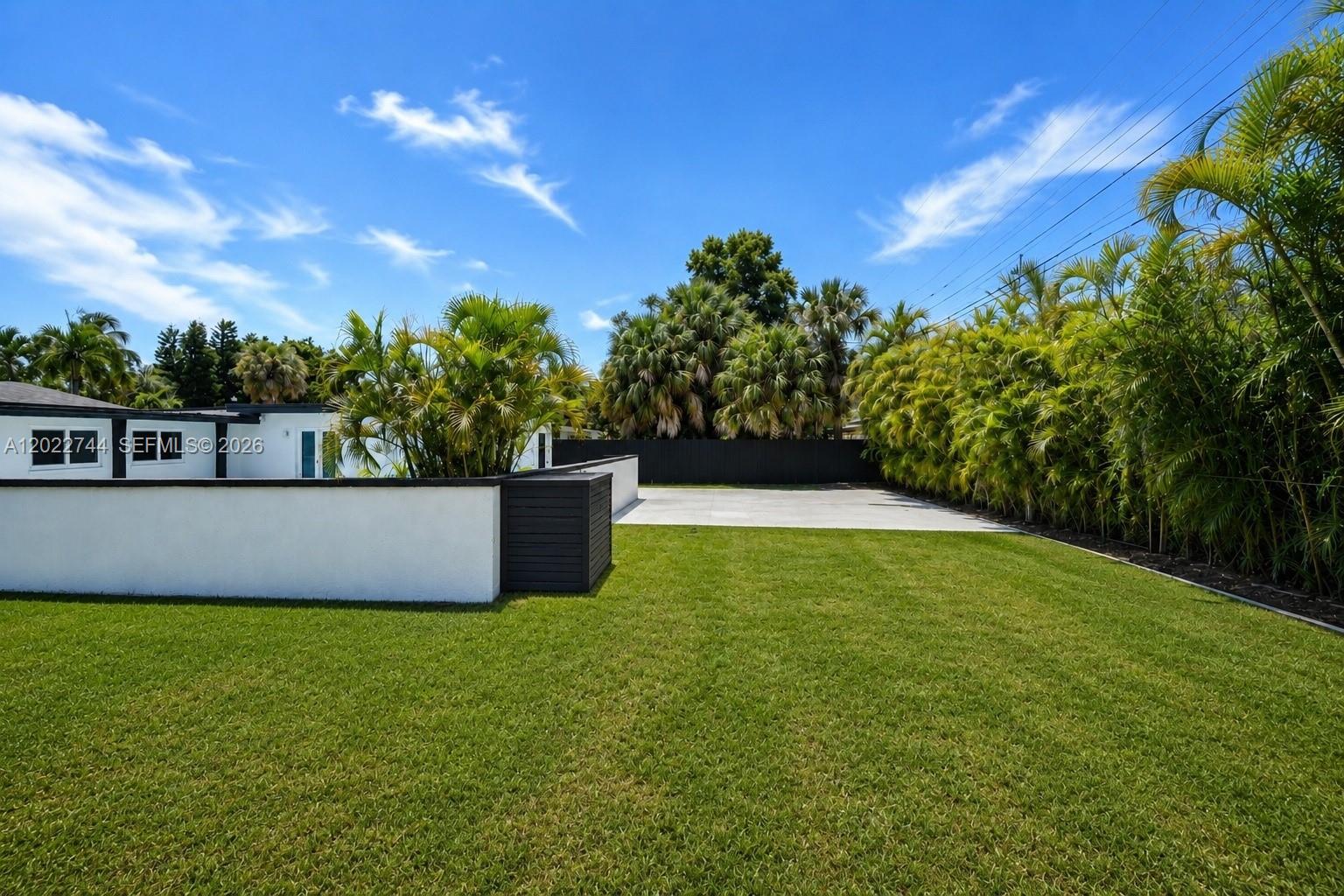 A grassy backyard features a white stucco wall, a concrete patio, and surrounding palm trees — 2573 Conroy Dr, North Palm Beach FL 33403, NORTH PALM BEACH, FL