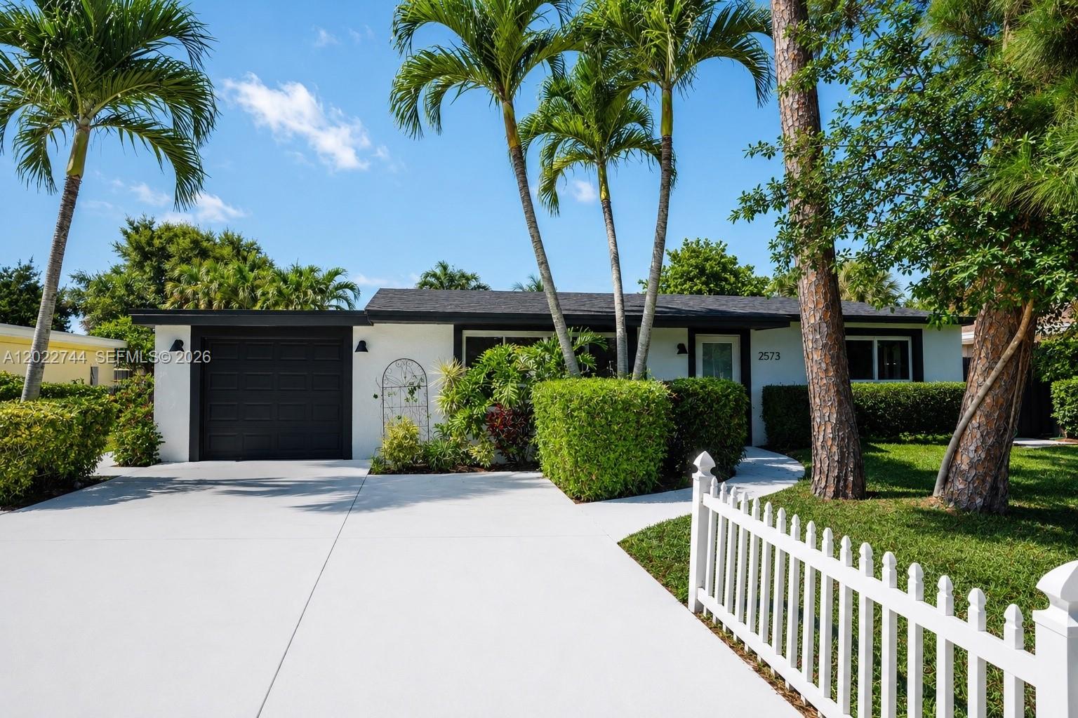 A single-story white house with a black garage door and a white picket fence — 2573 Conroy Dr, North Palm Beach FL 33403, NORTH PALM BEACH, FL