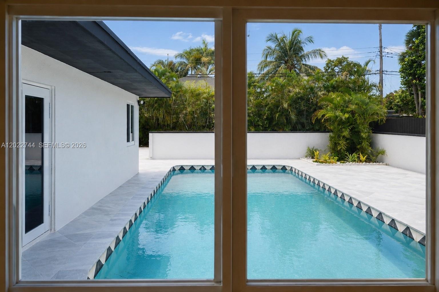 A rectangular swimming pool with decorative tile trim sits in a white-tiled backyard patio — 2573 Conroy Dr, North Palm Beach FL 33403, NORTH PALM BEACH, FL