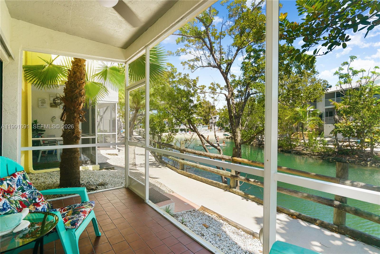 A screened-in porch features a tiled floor, a turquoise chair, and a view of a canal — 1500 Ocean Bay Dr # F5, Key Largo FL 33037, KEY LARGO, FL