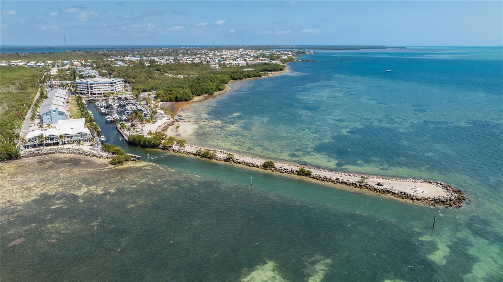 An aerial view shows a marina, a long stone jetty, and coastal buildings by the ocean — 1500 Ocean Bay Dr # F5, Key Largo FL 33037, KEY LARGO, FL