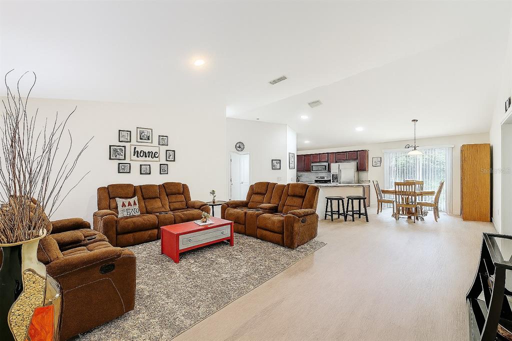 An open-concept living room and dining area with brown reclining sofas and a red coffee table — 6188 E SENECA STREET, INVERNESS, FL