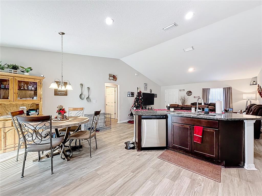 An open-concept kitchen and dining area features wood-look flooring, dark cabinetry, and vaulted ceilings — 6188 E SENECA STREET, INVERNESS, FL