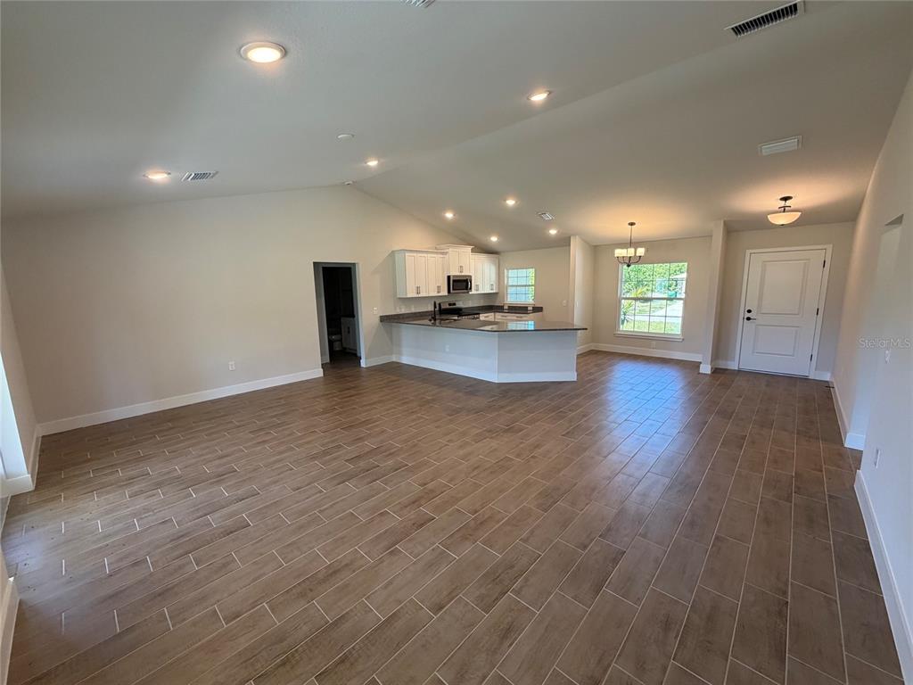 An open-concept living area features wood-look tile flooring, a kitchen with white cabinets, and recessed lighting — 871 RED BAY STREET, PORT CHARLOTTE, FL
