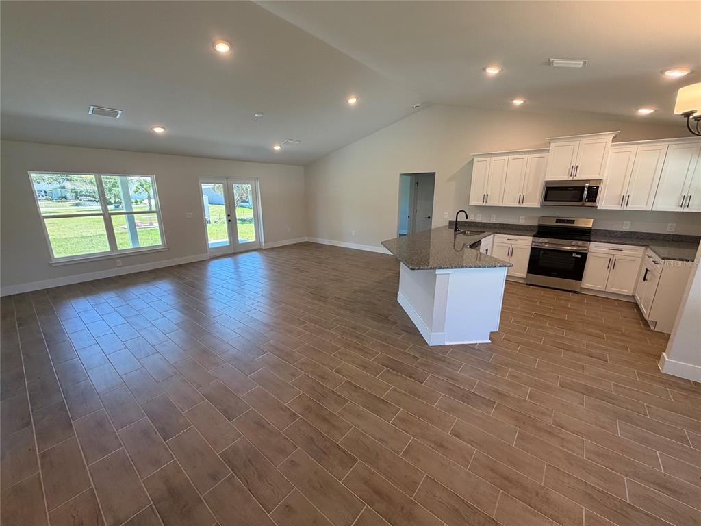 An open-concept kitchen and living area features wood-look tile flooring, white cabinets, and granite countertops — 871 RED BAY STREET, PORT CHARLOTTE, FL