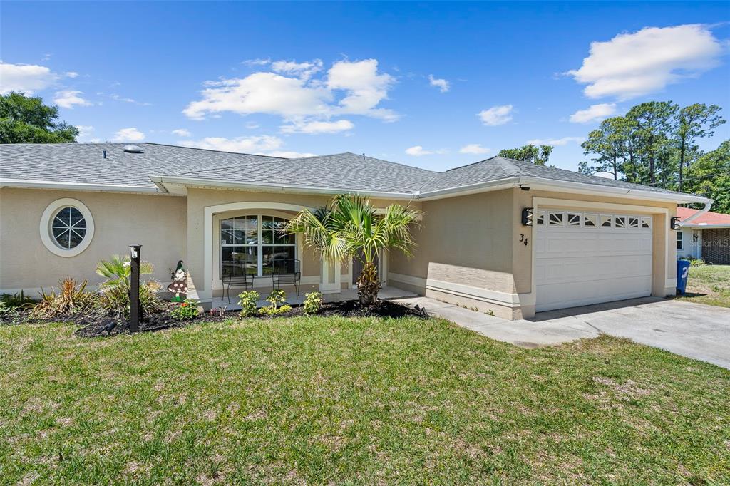 A single-story house with a beige stucco exterior, a two-car garage, and a front porch — 34 BEAVERDAM LANE, PALM COAST, FL