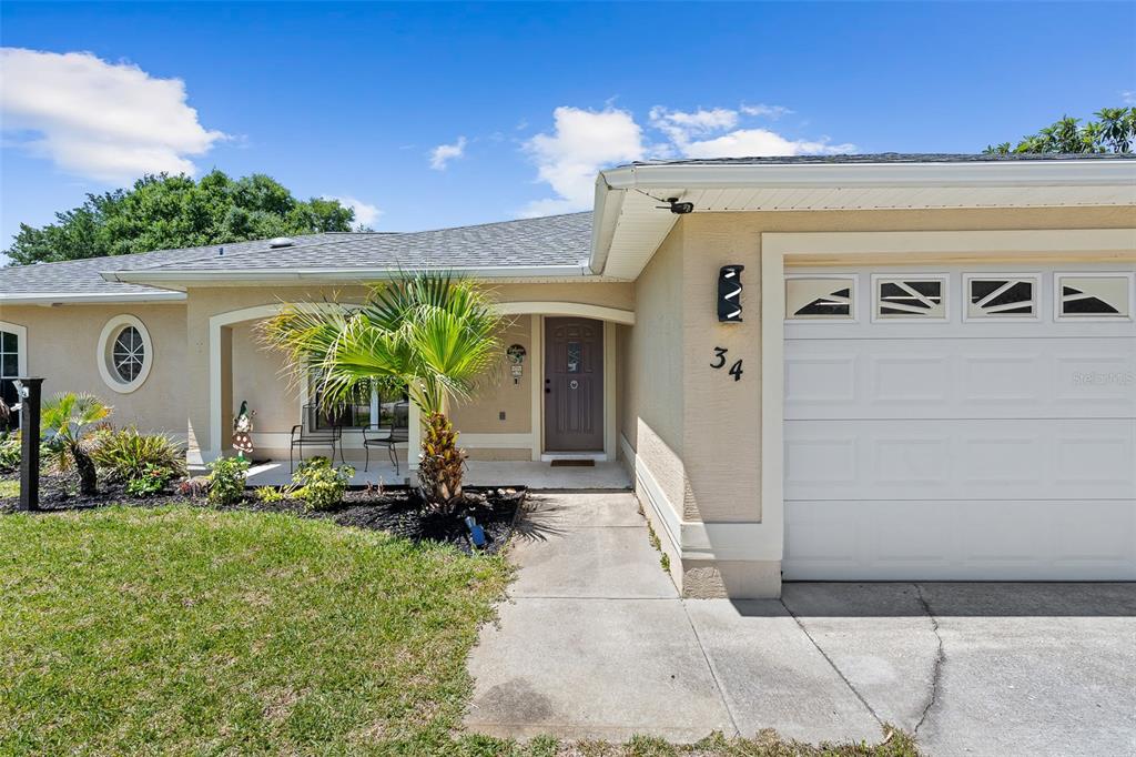 A beige single-story house features a white garage door, a front porch, and landscaping — 34 BEAVERDAM LANE, PALM COAST, FL