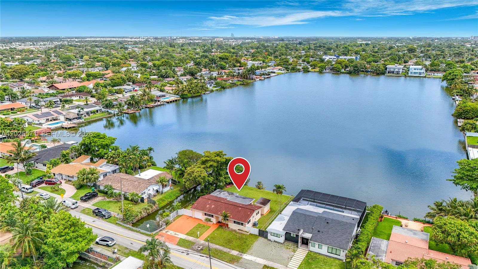 An aerial view shows a waterfront house with a red-tiled roof beside a large lake — 2501 NE 209th Ter, Miami FL 33180, MIAMI, FL