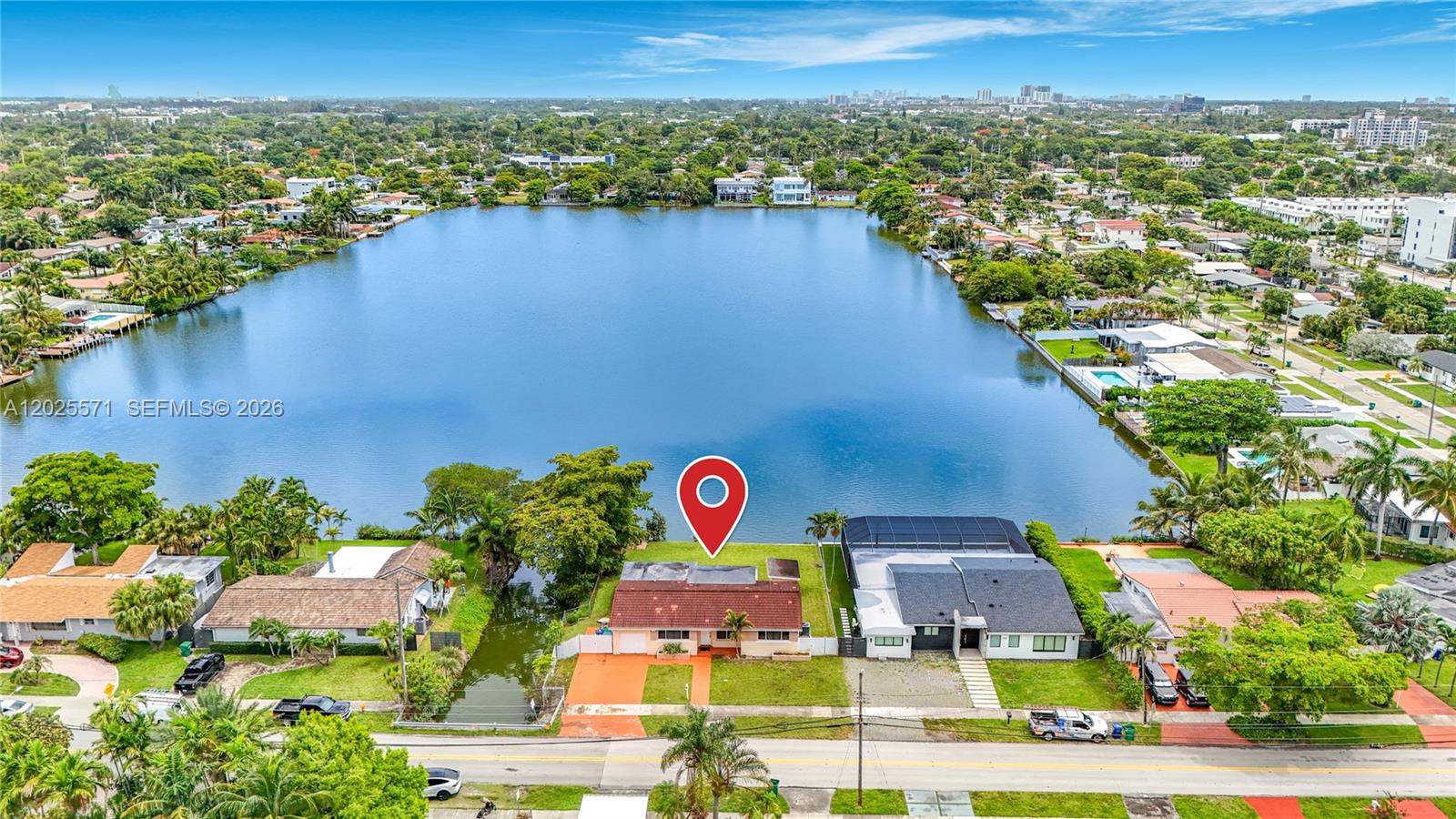 An aerial view shows a single-story house with a red roof situated beside a lake — 2501 NE 209th Ter, Miami FL 33180, MIAMI, FL