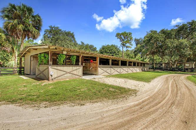 A long, wooden horse stable with an open-air design sits beside a dirt driveway — 2833 F Road, FL 33470, FL