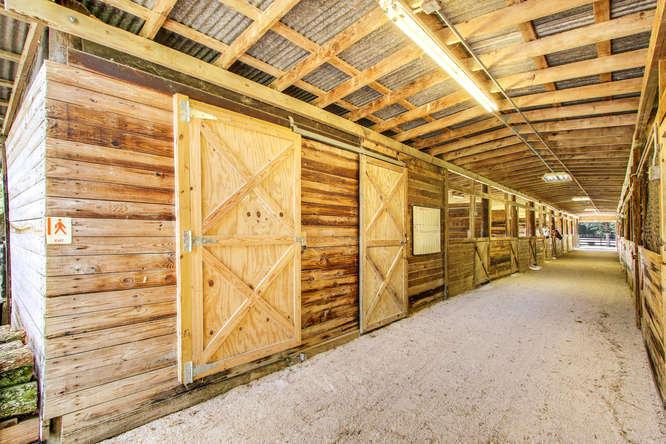 A long stable aisle features wooden stalls with sliding doors and a corrugated metal roof — 2833 F Road, FL 33470, FL
