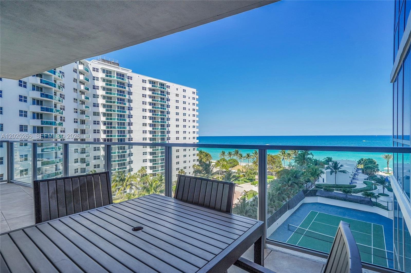 A balcony with a dining set overlooks a tennis court, palm trees, and the ocean — 3101 S Ocean Dr # 701, Hollywood FL 33019, HOLLYWOOD, FL