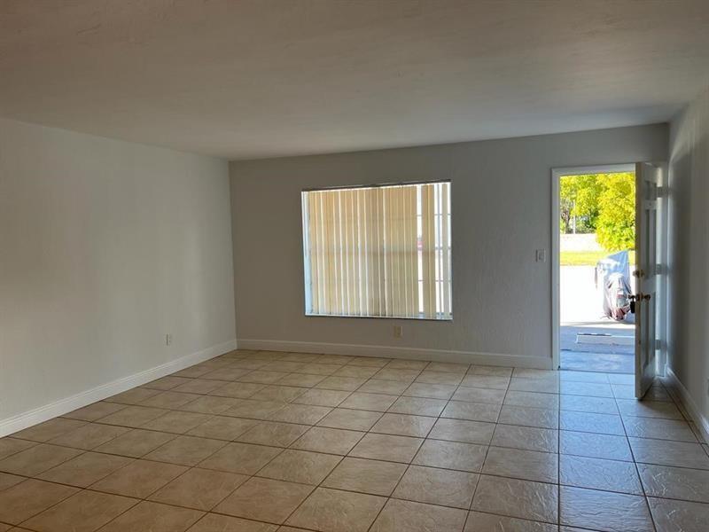An empty room with beige tile flooring, a large window with vertical blinds, and an open door — 7851 Dunham Boulevard # 4, Miami FL 33138, MIAMI, FL
