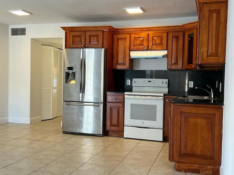 A kitchen with wooden cabinets, stainless steel refrigerator, white stove, and light-colored tile flooring — 7851 Dunham Boulevard # 4, Miami FL 33138, MIAMI, FL