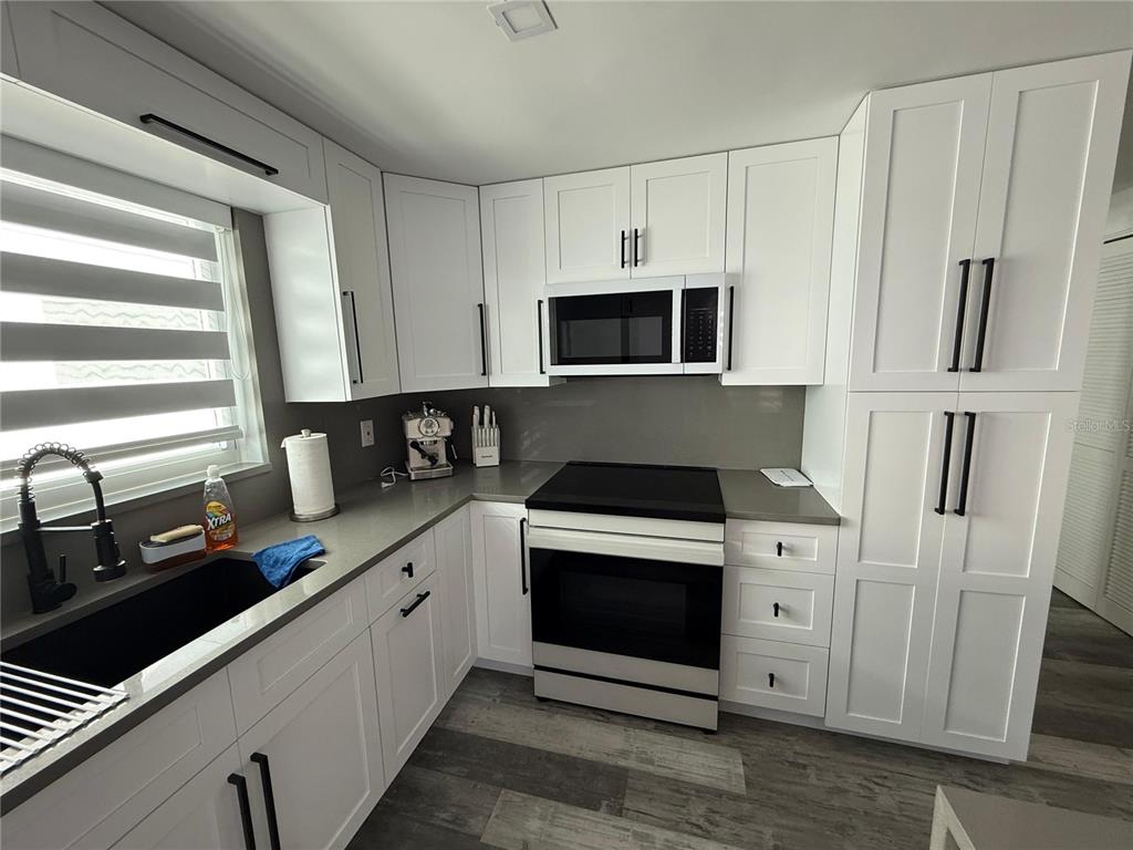 A modern kitchen features white cabinets, stainless steel appliances, and gray countertops — 5925 BEVERLY DRIVE, HUDSON, FL
