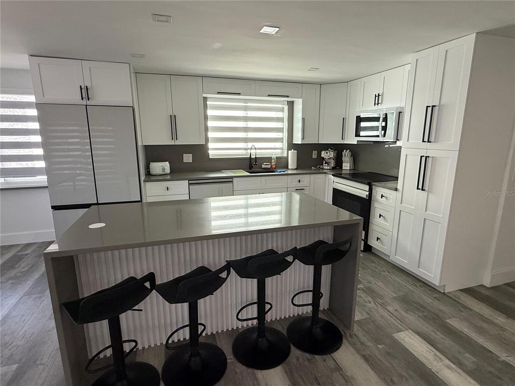 A modern kitchen features white cabinets, a gray island with bar stools, and stainless appliances — 5925 BEVERLY DRIVE, HUDSON, FL