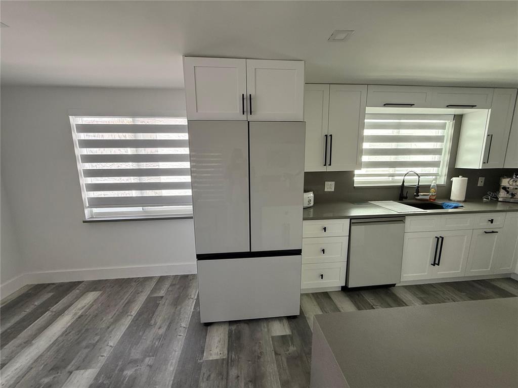 A kitchen features white cabinets, a stainless steel refrigerator, grey countertops, and wood-look flooring — 5925 BEVERLY DRIVE, HUDSON, FL