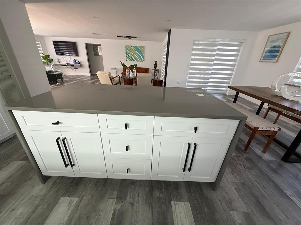 A kitchen island with white cabinets and a gray countertop sits in an open-concept room — 5925 BEVERLY DRIVE, HUDSON, FL