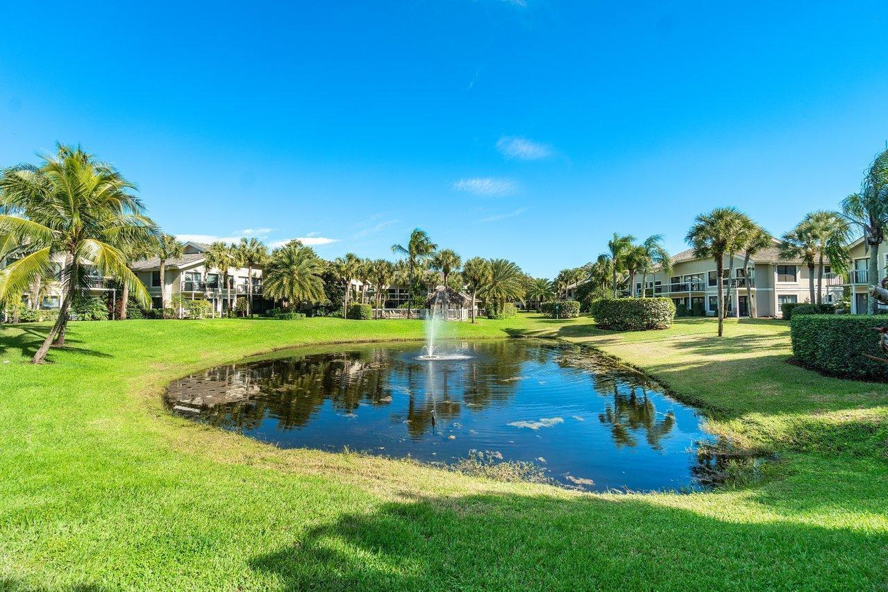 A pond with a central fountain sits in front of multi-story apartment buildings and palm trees — 11863 Wimbledon Circle # 445, Wellington FL 33414, WELLINGTON, FL