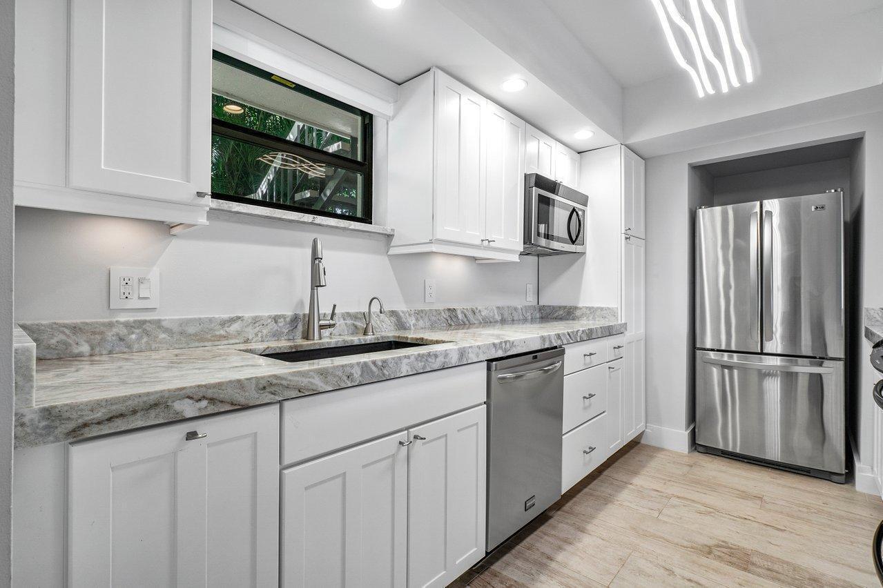 A modern kitchen features white cabinetry, marble-patterned countertops, stainless steel appliances, and wood-look flooring — 11863 Wimbledon Circle # 445, Wellington FL 33414, WELLINGTON, FL