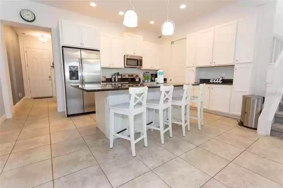 A kitchen with white cabinets, a stainless steel refrigerator, and a central island with stools — 134 CAPTIVA DRIVE, DAVENPORT, FL