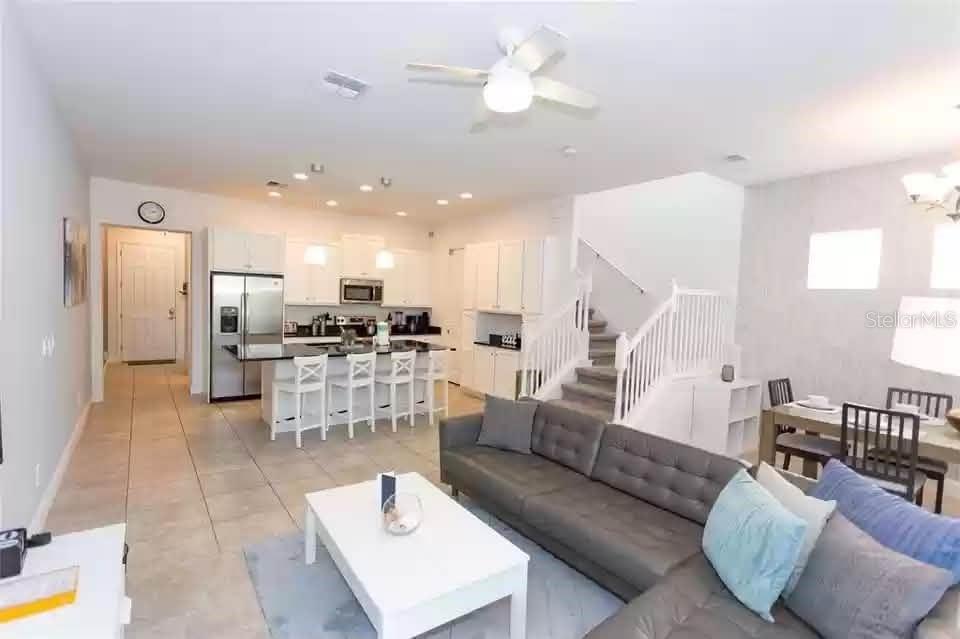 An open-concept living area features a kitchen with white cabinets, a sofa, and stairs — 134 CAPTIVA DRIVE, DAVENPORT, FL