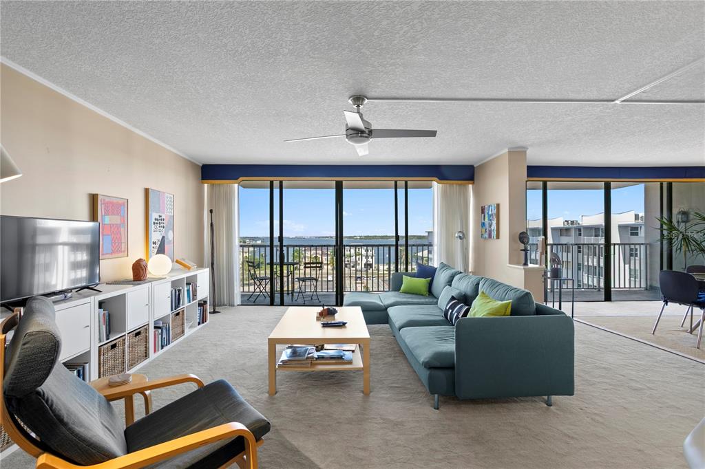 A living room features a blue sectional sofa, a coffee table, and a balcony view — 450 TREASURE ISLAND CAUSEWAY UNIT 702, TREASURE ISLAND, FL
