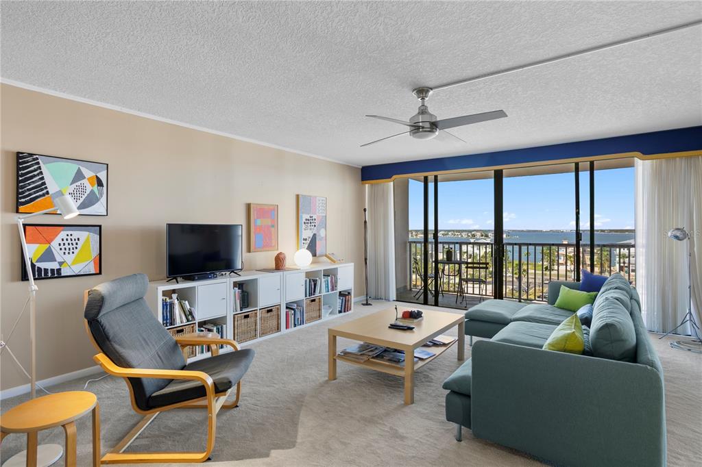 A living room features a blue sectional sofa, a gray armchair, and a balcony view — 450 TREASURE ISLAND CAUSEWAY UNIT 702, TREASURE ISLAND, FL