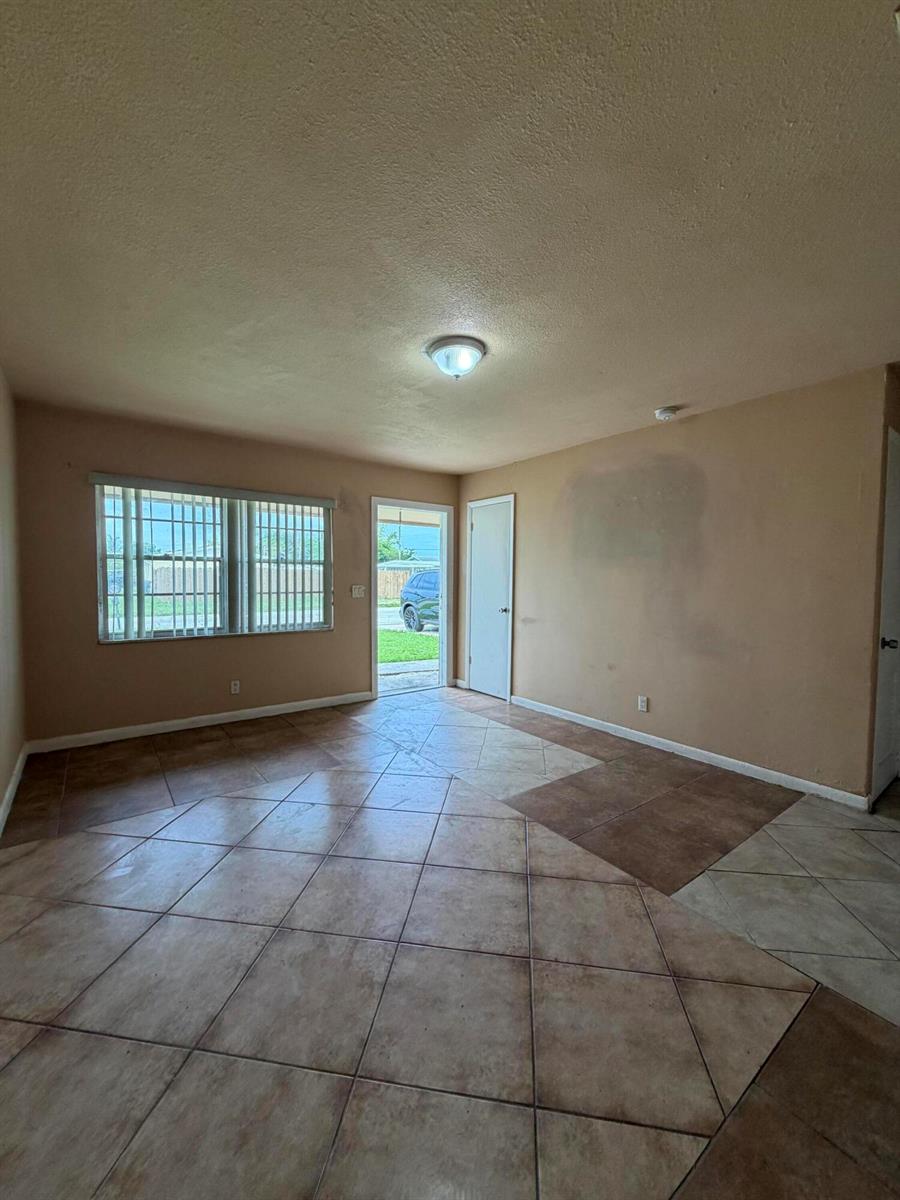 An empty room features tan walls, a single ceiling light, and diagonal brown tile flooring — 3243 Grove Road, Boynton Beach FL 33435, BOYNTON BEACH, FL